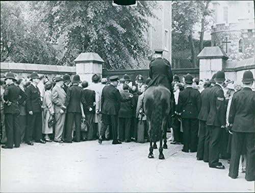 Vintage fotografija grupe ljudi koji su udubili policajci ispred kapije zgrade.